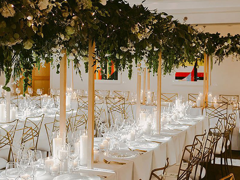 Davis Commons with gold wire-backed seating, gold utensils, large garland with soft lighting, and glassware with candles